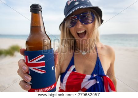 Australian Woman On The Beach Holding Or Offering A Beer And Cheerfully Smiling.  Focus To Bottle Wh