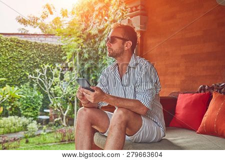 Man Using Smart Phone On A Terrace Sofa In Summertime.