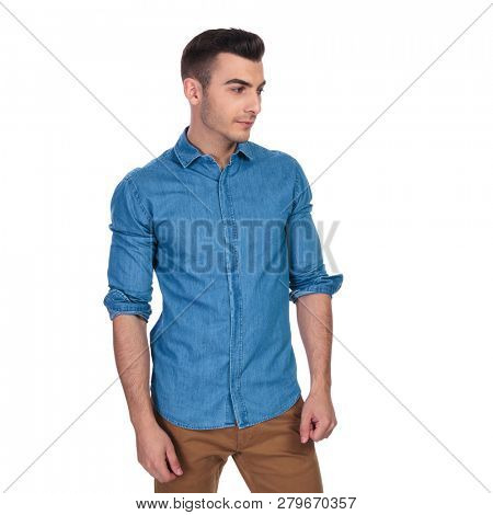 portrait of curious casual man looking down to side while standing on white background with rolled sleeves