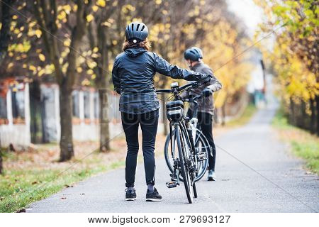 Active Senior Couple With Electrobikes Standing Outdoors On A Road In Park.