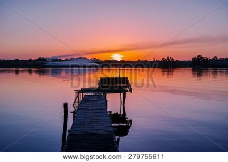 River Bridge For Fishing On The Background Of Sunset And Smoke Above The Water.