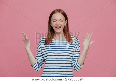 Waist Up Shot Of Overjoyed Pretty Woman Gestures With Hands, Laughs Positively, Being In High Spirit