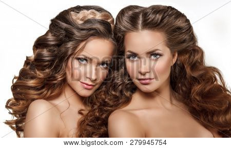 Beautiful models twins girls with shiny brown straight long hair. Women with Perfect Health Skin face smiling. Care and updo hair products. Youth, Spa and Skin Care Concept