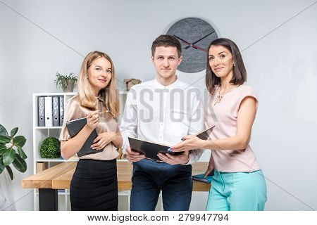 Theme Business, Teamwork And Partnerships. A Group Of Young People, Three People, Stand In An Office