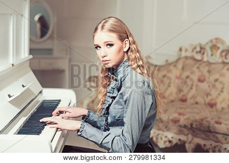 Young Victorian Girl In A Tender Blue Dress Learning To Play Piano. Lovely Blond With Curly Hair Wom