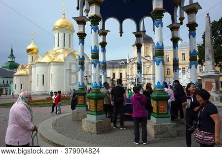 Sergiyev Posad, Russia - June 26, 2019: Russian old woman babushka and chinese tourists at Holy water spring under colorful canopy at Trinity Lavra of St. Sergius