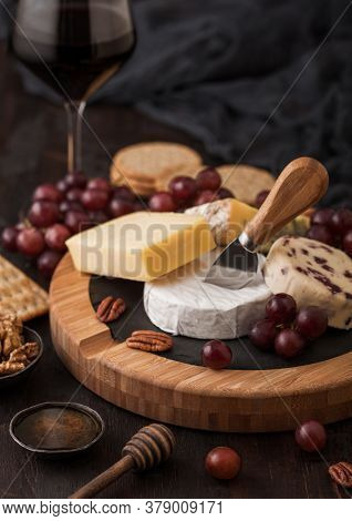 Glass Of Red Wine With Selection Of Various Cheese On The Board And Grapes On Wooden Table Backgroun