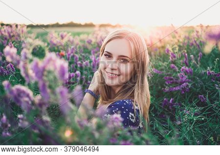 Smiling Girl Walks On Tall Grass Overgrown With Purple Flowers
