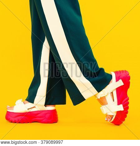 Women's Legs In Sport Sandals With Red Soles And Green Pants With Stripes On A Yellow Background.