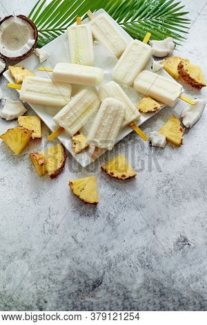Summer popsicles on stick. Pinacolada flavour. Made with pineapple, cocount milk and rum. Vegan snack. Decorated with fresh fruit. Top view. Flat lay.