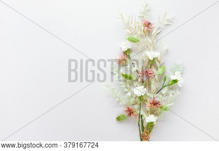 Flower composition made of dried light-green leaves of ruscus and white flowers on pastel grey background. Nature concept, copy space, flat lay.