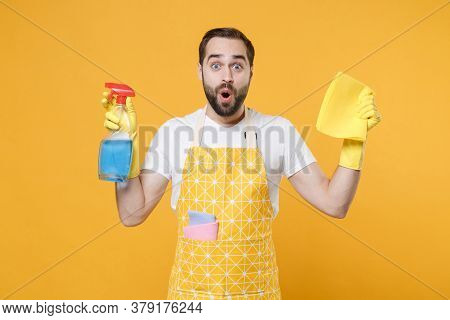 Shocked Young Man Househusband In Apron Rubber Gloves Hold Spray With Washing Cleanser, Cleaning Rag