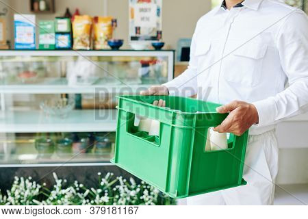 Cropped Image Of Delivery Man In White Uniform Carrying Plastic Milk Crate To The Grocery Store