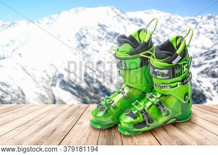 Ski Boots On A Wooden Table Against The Background Of Mountains. Bright Green Sports Ski Boots