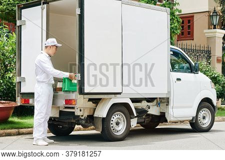 Delivery Man In White Uniform Taking Plastic Crate With Glass Milk Bottles Out Of Van Trunk