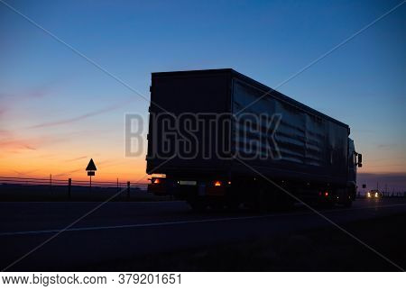 A Cargo Truck Drives On The Motorway In The Evening Against The Backdrop Of Sunset. Truck Logistics 