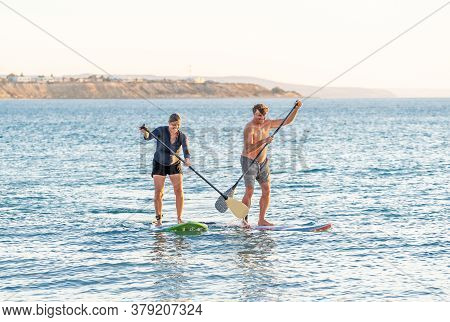 Mature Couple On Sup, Stand Up Paddle Board, Having Fun On Quiet Sea At Sunset