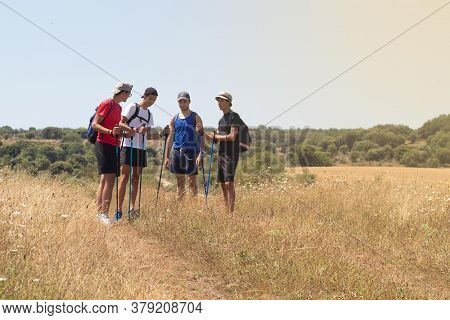 Young People Talking During A Walk With The Trekking Sticks Through The Countryside And The Camino D