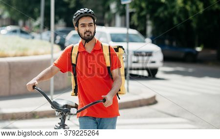 Delivery To Home Or Office. Young Man With Beard In Protective Helmet With Large Yellow Backpack Wit