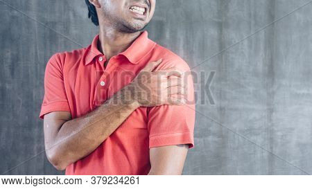 Young Asian Man Suffering Shoulder Pain On Cement Wall Background With Copy Space, Problems And Heal