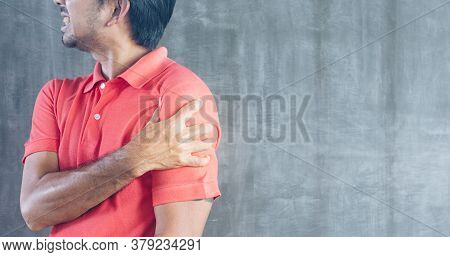 Young Asian Man Suffering Shoulder Pain On Cement Wall Background With Copy Space, Problems And Heal