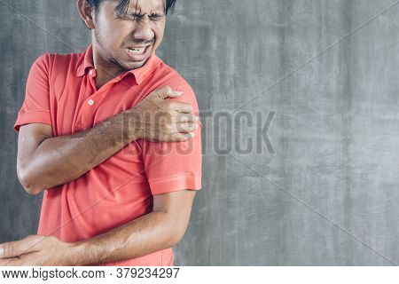 Young Asian Man Suffering Shoulder Pain On Cement Wall Background With Copy Space, Problems And Heal