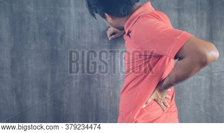 Hand Of Man Touching Her Back Pain On Cement Wall Background With Copy Space, Problems And Health Ca
