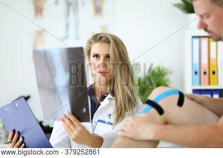 Doctor Woman With Examines An X-ray Of Leg Next To Patient Sits. Medical Service Concept