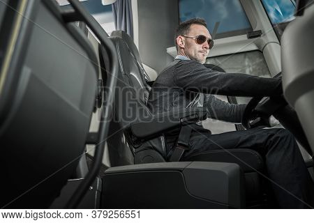 Caucasian Male Coach Bus Driver In His 40s Behind Vehicle Steering Wheel. Public Transportation Them