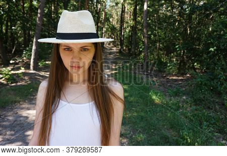 A Young, Pretty Girl, In White Clothes, And A White Hat, Insolently Looks At The Camera, In The Back