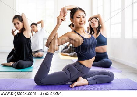 Portrait of asian yoga instructor coach wearing sportswear bra pants do king pigeon pose in yoga studio with her students in background. Work out fitness healthy lifestyle concept.