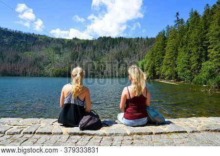Two women sitting by Black lake (Cerne jezero) in the National park Sumava, Czech Republic.