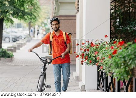 Active Physical Work In City. Guy Curier With Beard With Yellow Backpack In Protective Helmet, Holds