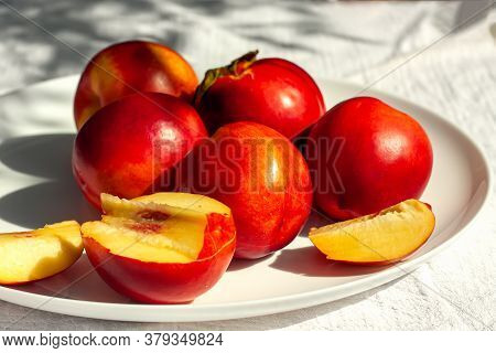 Red Ripe Organic Nectarine Fruits On The White Plate On Nature Background. Summertime Healthy Eating