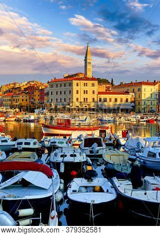 Rovinj, Istria, Croatia. Motorboats and boats on water in port Rovigno. Medieval vintage houses of old town. Yachts landing, high tower of Church of Saint Euphemia. Morning sunrise blue sky.