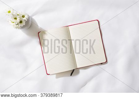 Top view of morning scene in voile fabric background with a red notebook in the middle and a vase of