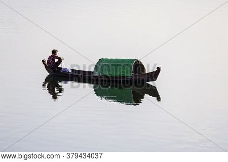 Mandalay/myanmar-october 6th 2019: A Burmese Fisherman Sits On A Wooden Fishing Boat And Uses A Net 