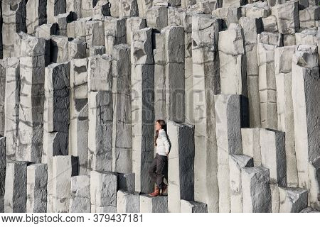 Iceland tourist at beach sitting on basalt columns on Reynisfjara beach, the black sand beach of Vik, South Iceland coast. Happy woman visiting tourist attraction destination.