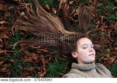 Teengirl laying on autumn ground - long hair scattered on grass.