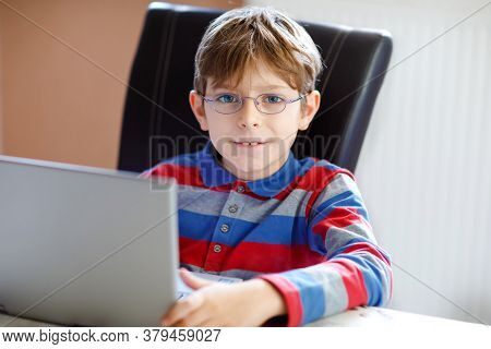 Happy Healthy Kid Boy With Glasses Making School Homework At Home With Notebook. Interested Child Wr