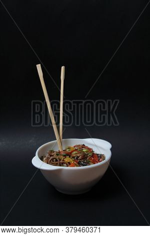 A Bowl Of Wok Noodles And Chopsticks Isolated On Black Background. Vertical Image. Image Contains Co