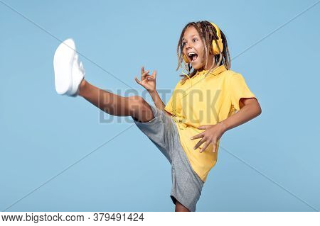 Happy Little Boy With African Dreads Listening Music In Headphones Dancing Over Blue Background.