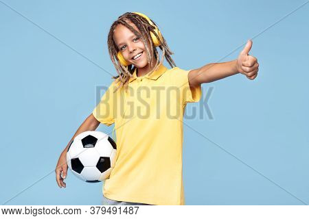 Funny Little Boy With African With Headphones Holding Soccer Ball And Show Thumb Up Over Blue Backgr