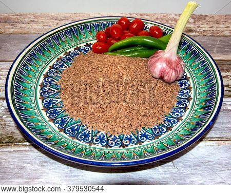 Raw Brown Rice Of Devzira For Uzbek Pilaf On A Beautiful Dish With An Ornament, On The Side Are Cher