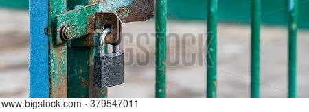 Closed And Locked Door Grill With Silver Padlock. A Metal Lock On Hinges Hangs In Close-up On The Gr