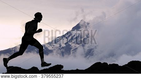 Running man athlete trail running in mountain summit background. Male runner on run training outdoors living active fit lifestyle. Silhouette at sunset.