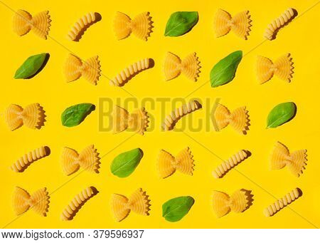 Uncooked Curly Pasta And Basil Leaf Pattern On Yellow Background. Traditional Dry Raw Macaroni Patte
