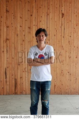 Man Wearing South Korea Flag Color Shirt And Cross One's Arm On Wooden Wall Background, White Color 