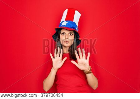 Young beautiful brunette woman wearing united states hat celebrating independence day Moving away hands palms showing refusal and denial with afraid and disgusting expression. Stop and forbidden.