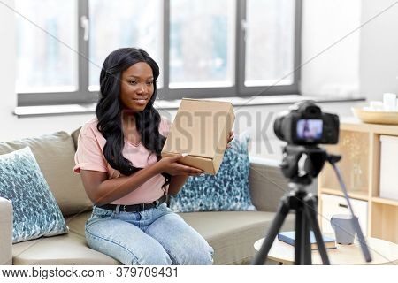 blogging, videoblog and people concept - african american female video blogger with parcel box and camera videoblogging at home